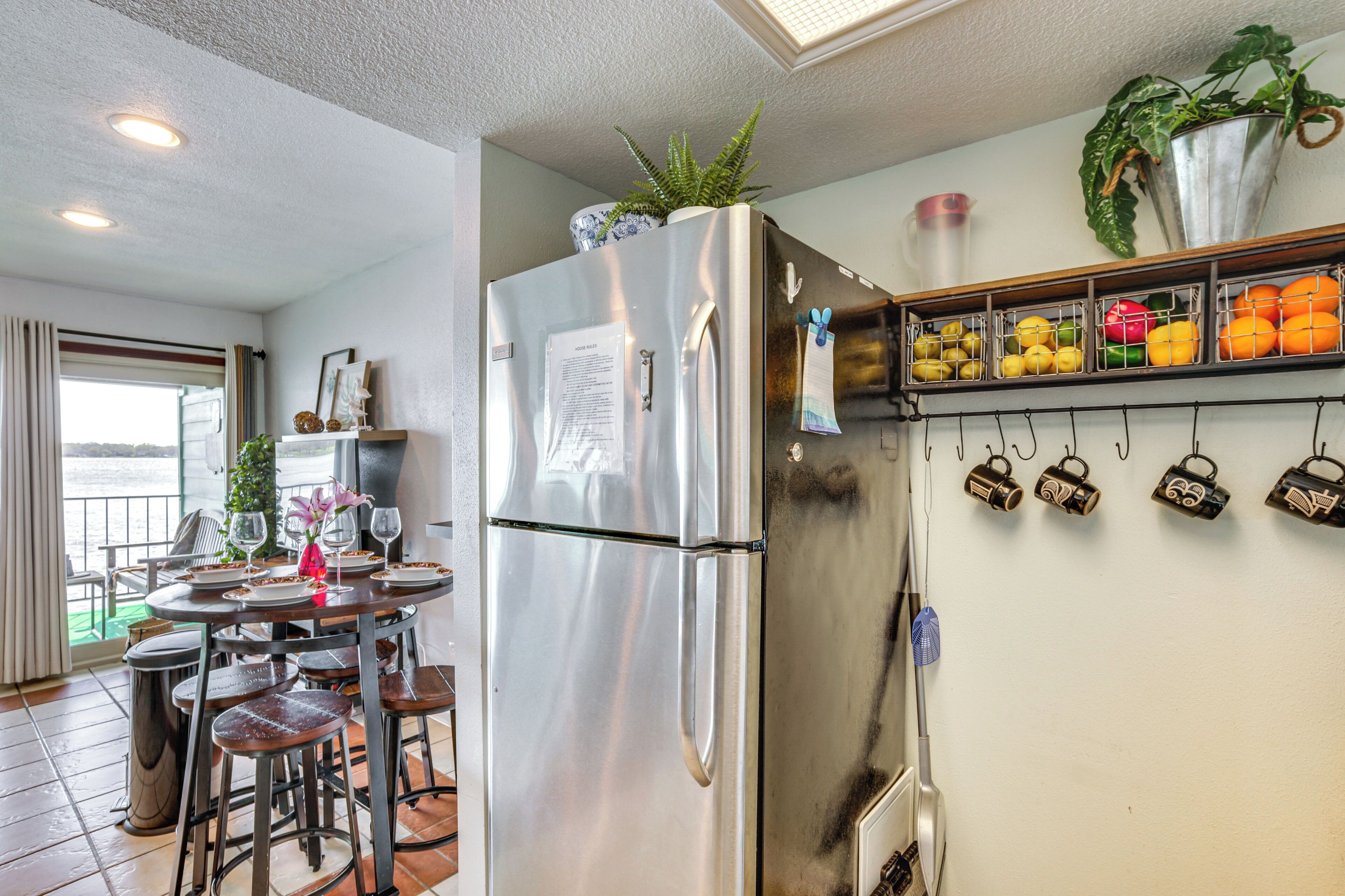 A modern kitchen with a stainless steel refrigerator, a dining area with bar stools, and a fruit display on the wall.