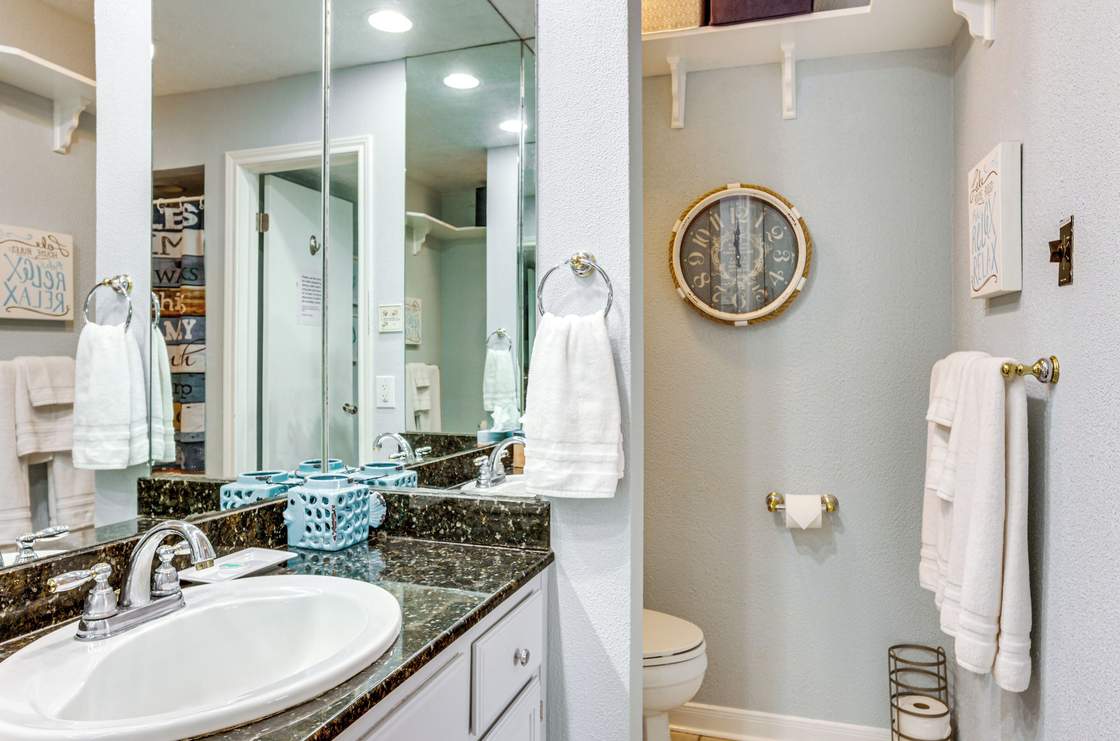 A bathroom with a sink, mirror, towel rack, toilet, and a clock on the wall.