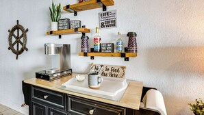 A kitchen with wooden shelves holding various items, a coffee machine, and a sign that reads "Life happens between coffee & wine." - Resort-style Lake Conroe Retreat w/ Balcony & View (Willis)