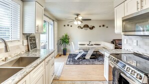 A modern kitchen with a granite countertop, stainless steel appliances, and a dining area with a white table and chairs.