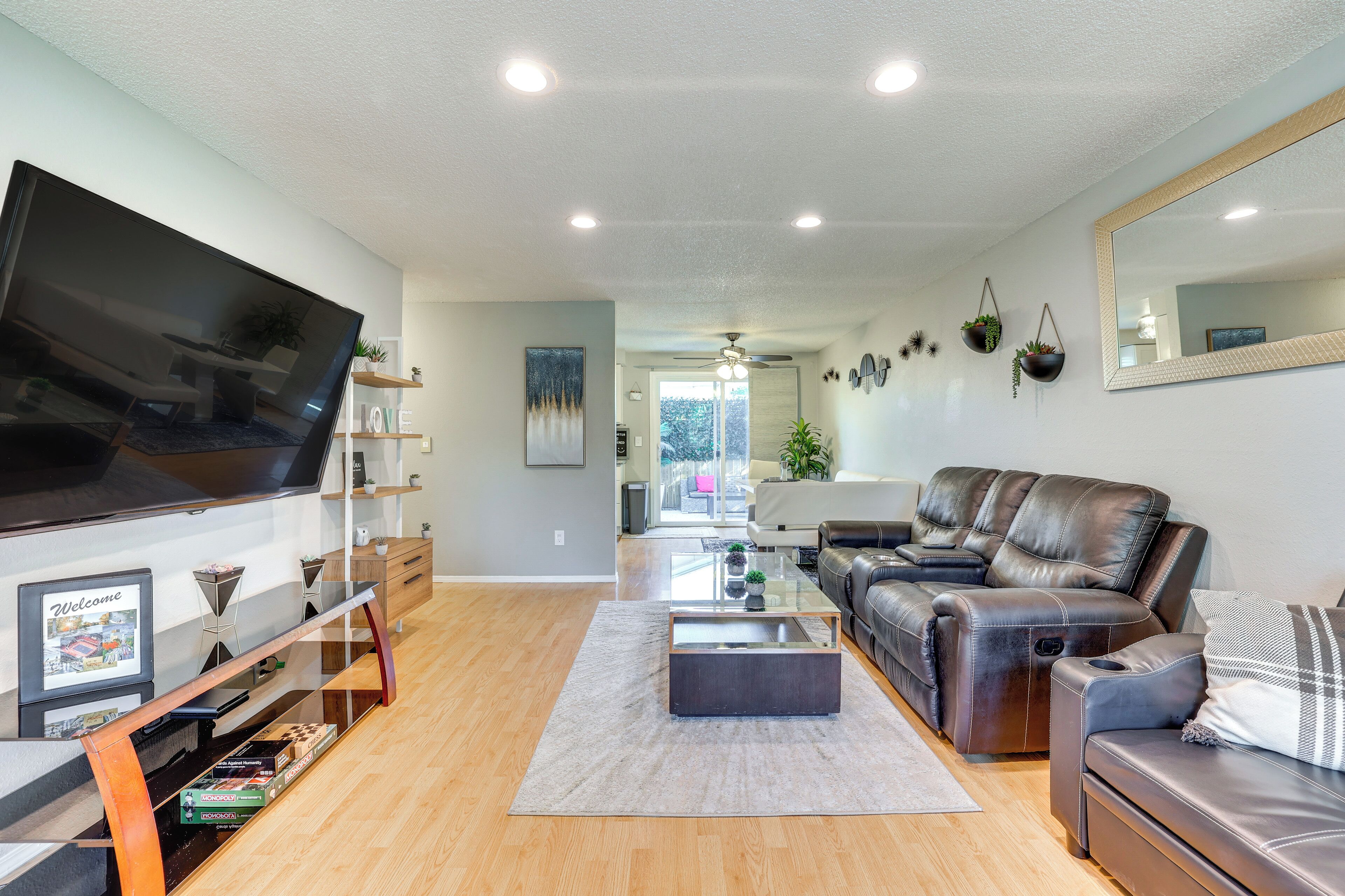 A modern living room with a flat-screen TV, leather sofas, a coffee table, and a large mirror.