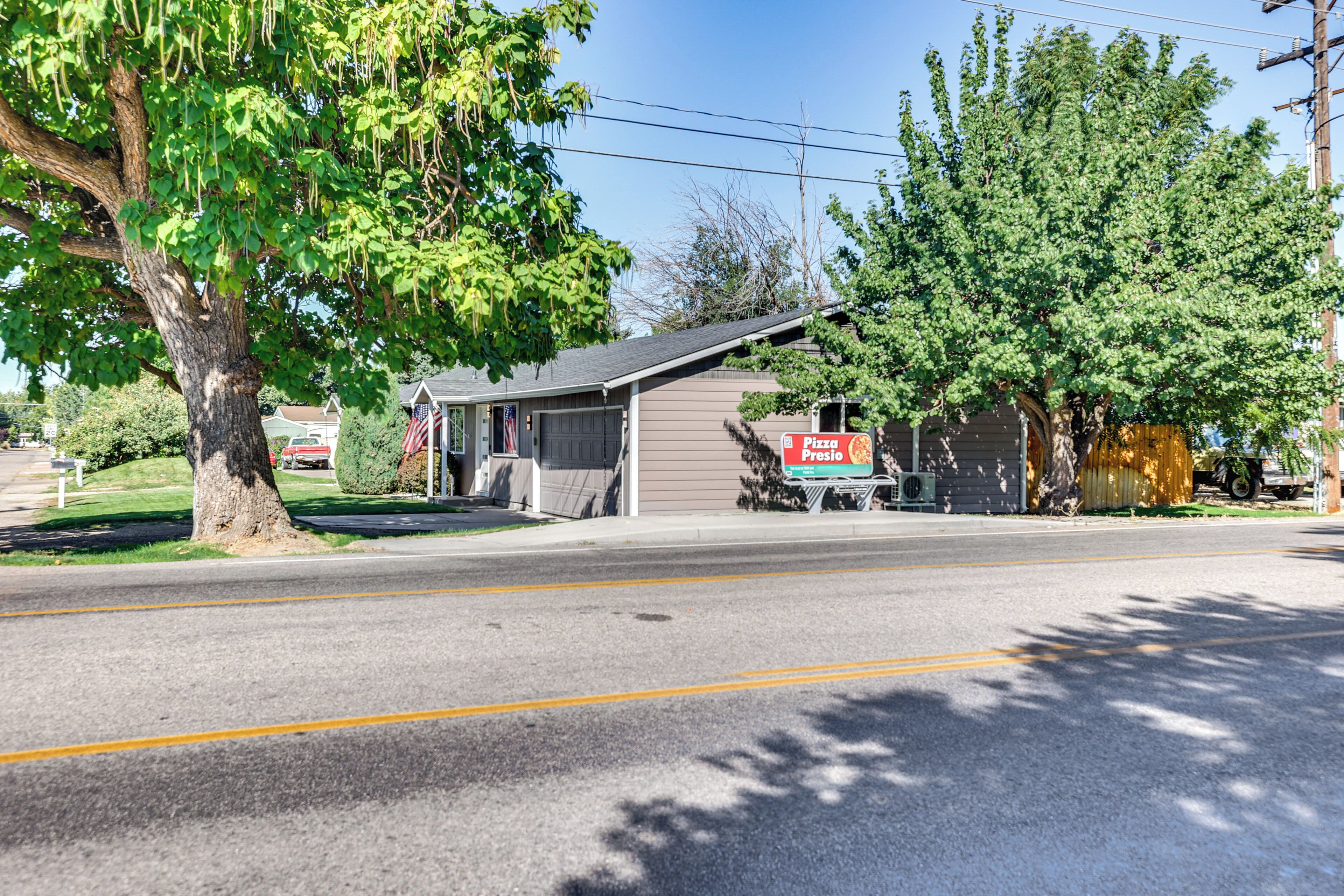 A street view with a building featuring a pizza sign, a garage, and a large tree.