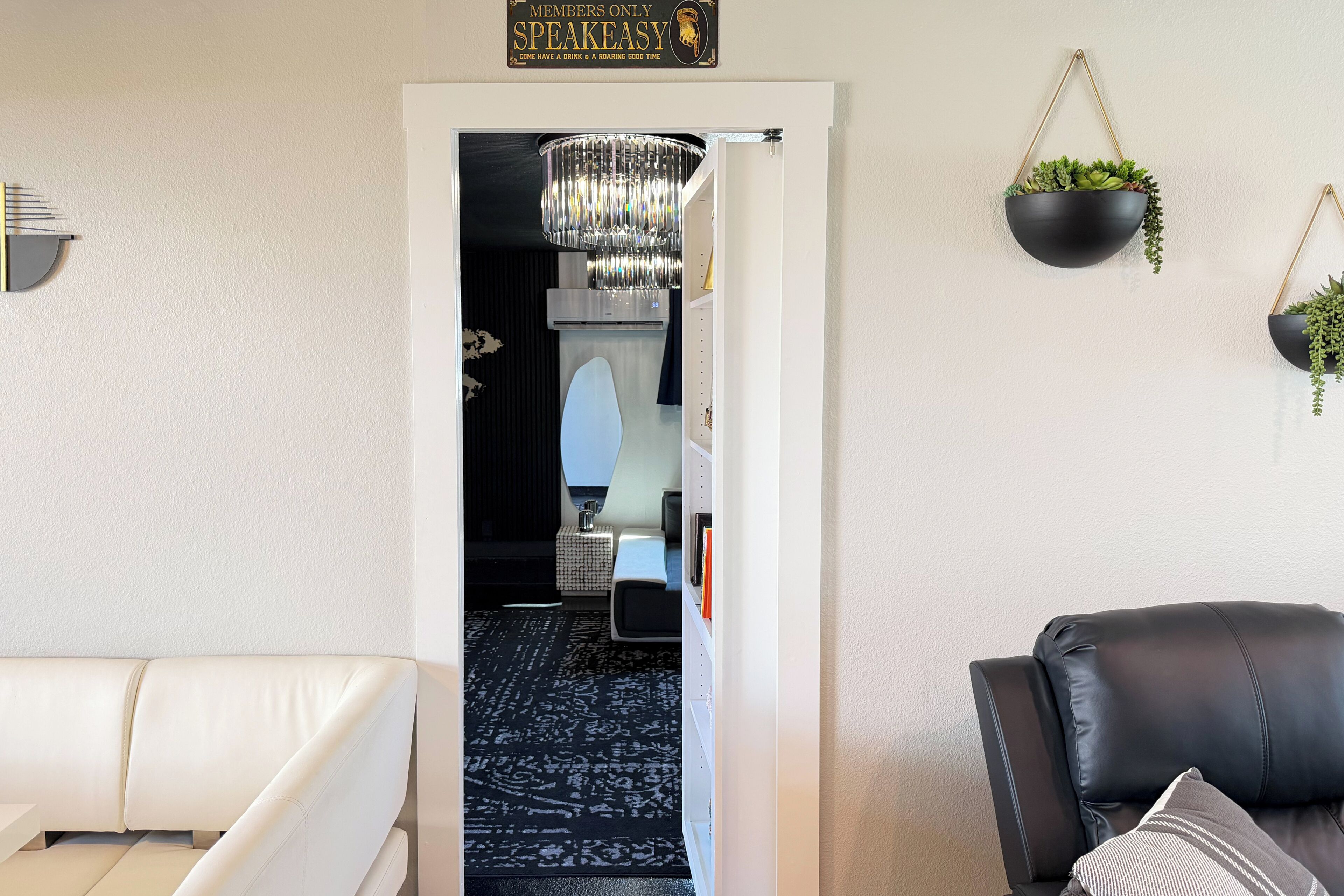 Ein modernes Wohnzimmer mit einem weißen Sofa, einem schwarzen Ledersessel, einer Chandelierleuchtre und einem Schild über der Tür.