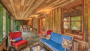 Een gezellig cabin interieur met houten wanden en plafond, een blauwe bank, een rode fauteuil, en een eethoek met houten tafels en stoelen.