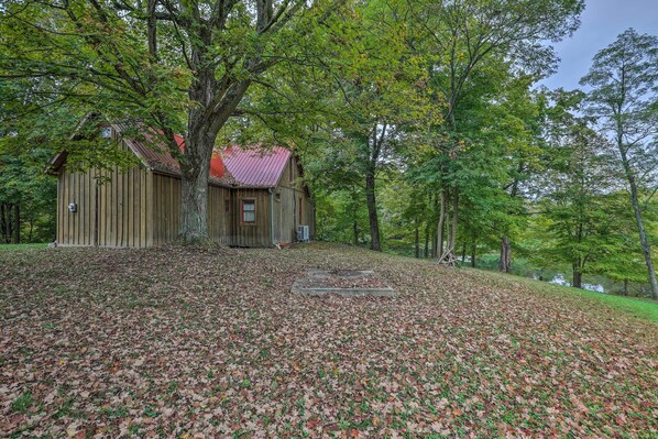A rustic wooden cabin with a red roof, surrounded by a forested area with a leaf-covered ground.