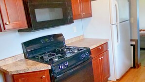A kitchen with wooden cabinets, a black microwave, a stove, and a white refrigerator. - Fantastic Oasis Home in Stevens Point with fully enclosed fence for backyard! (Stevens Point)