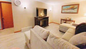 A living room with a sofa, a television, a painting, and a clock on the wall. - Fantastic Oasis Home in Stevens Point with fully enclosed fence for backyard! (Stevens Point)