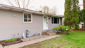 A single-story house with a front porch, a small garden area with plants and a bird feeder, and a tree to the right. - Fantastic Oasis Home in Stevens Point with fully enclosed fence for backyard! (Stevens Point)