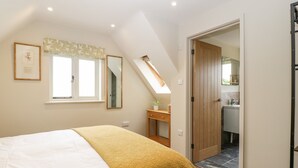 Un dormitorio con cama, mesita de noche, ventana con vistas, puerta que da a un baño y tragaluz.