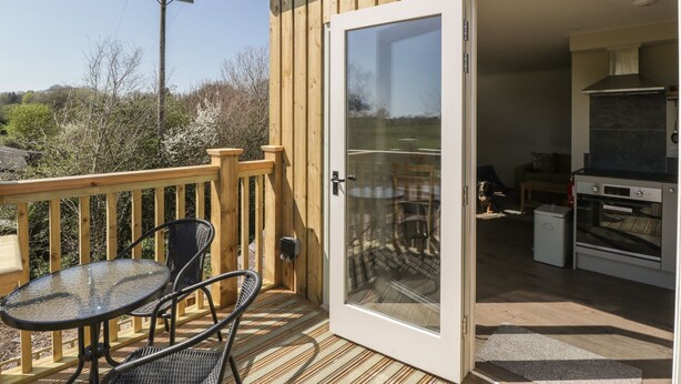 Una terraza de madera con un ventanal de vidrio que da a una zona de cocina con una parrilla y una mesa de comedor con sillas.