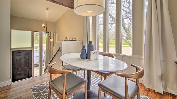 A dining area with a round table, four chairs, a hanging light fixture, and large windows with curtains. - Cozy Lake Geneva Retreat With Year-round Views! (Lake Geneva)