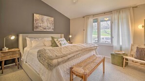 A bedroom with a bed, bedside table, lamp, bench, chair, and a window with curtains. - Cozy Lake Geneva Retreat With Year-round Views! (Lake Geneva)