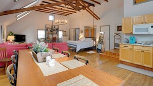 A spacious loft with a high ceiling, exposed wooden beams, a dining area with a wooden table, a kitchen with wooden cabinets, and a cozy living area with a sofa and a television. - Pet-friendly Loft Vacation Rental w/ Fire Pit! (Bemus Point)