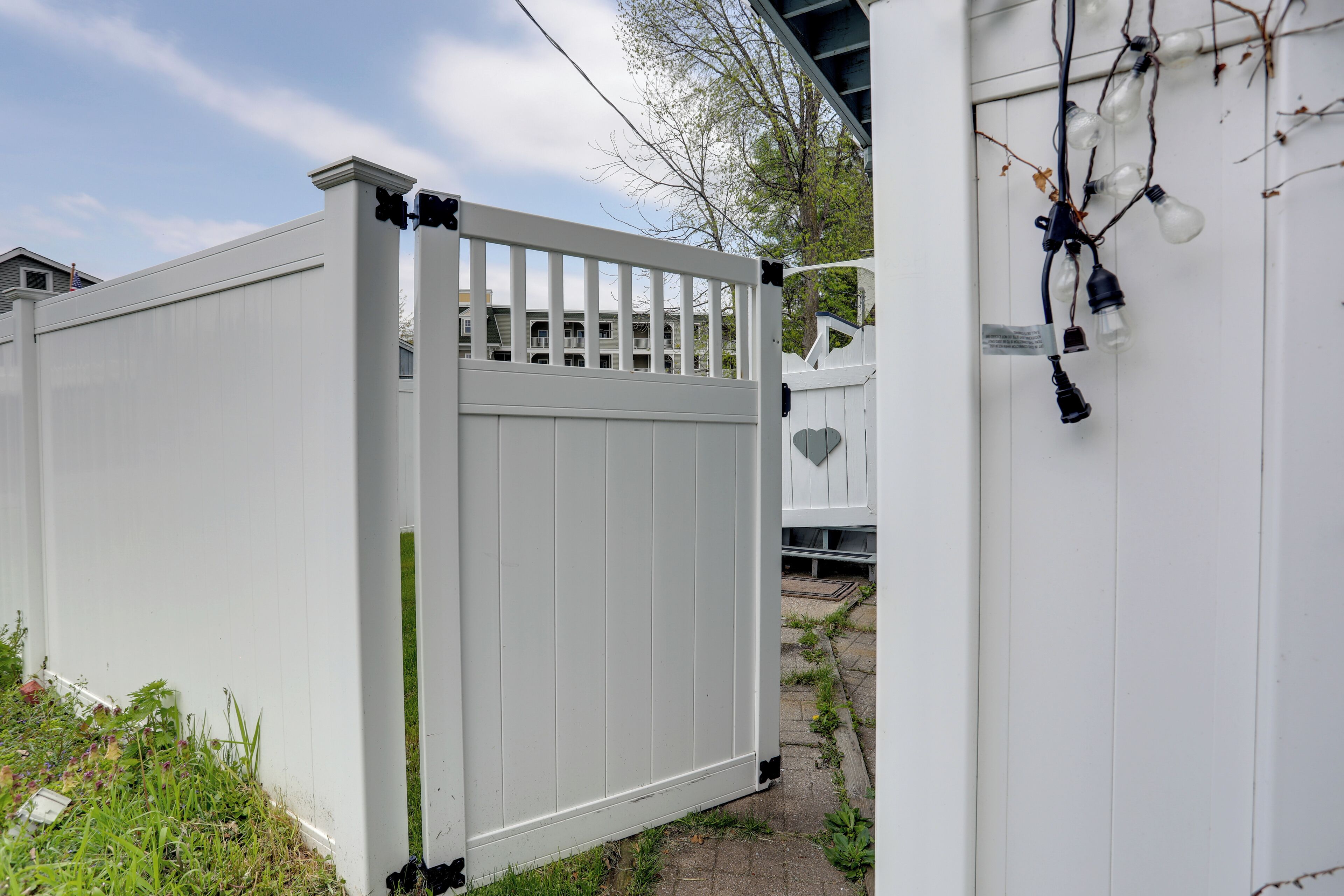 A white wooden gate with vertical slats, a white fence, and a small garden area with grass and plants.
