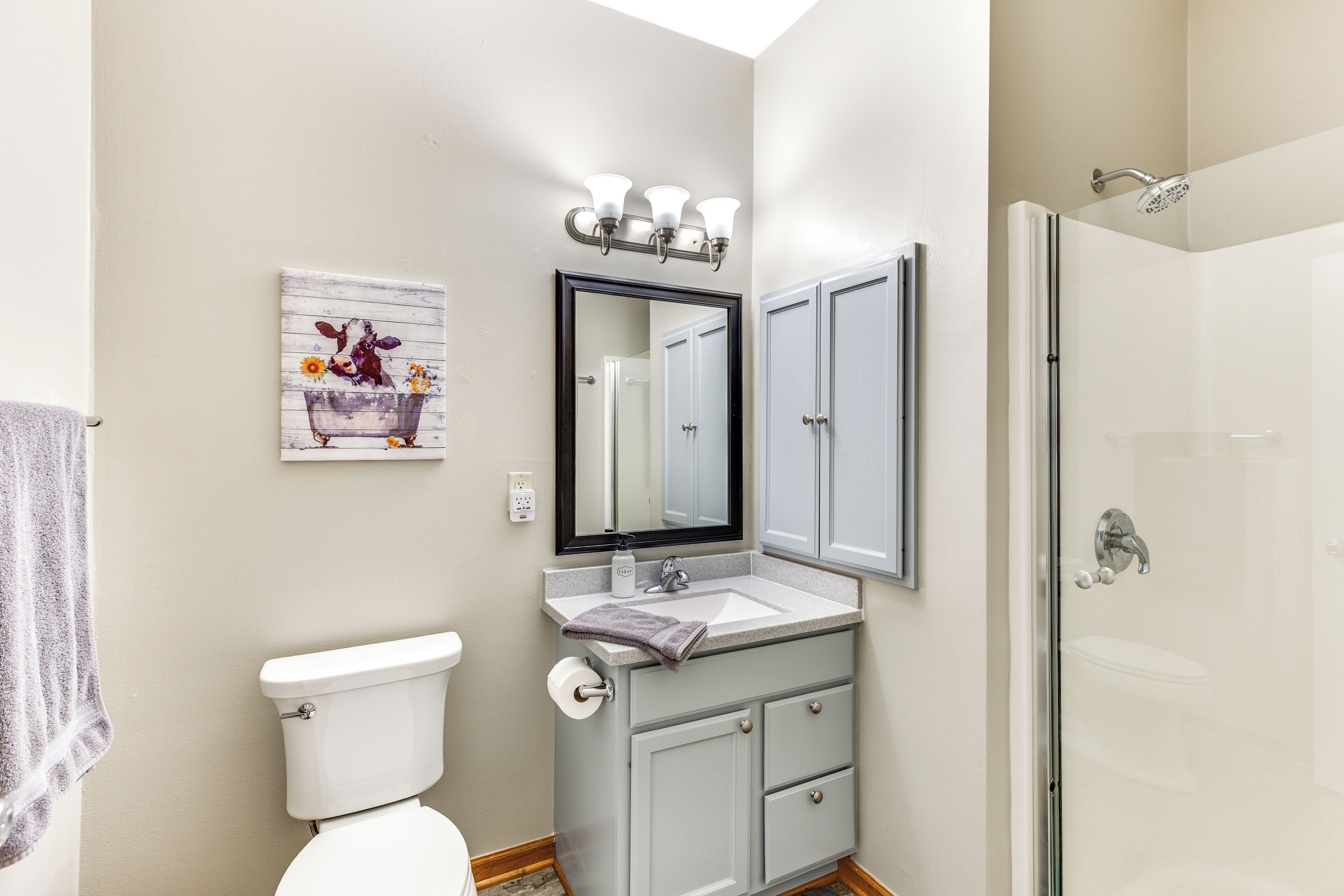 A bathroom with a toilet, sink, mirror, and shower.