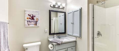 A bathroom with a toilet, sink, mirror, and shower.
