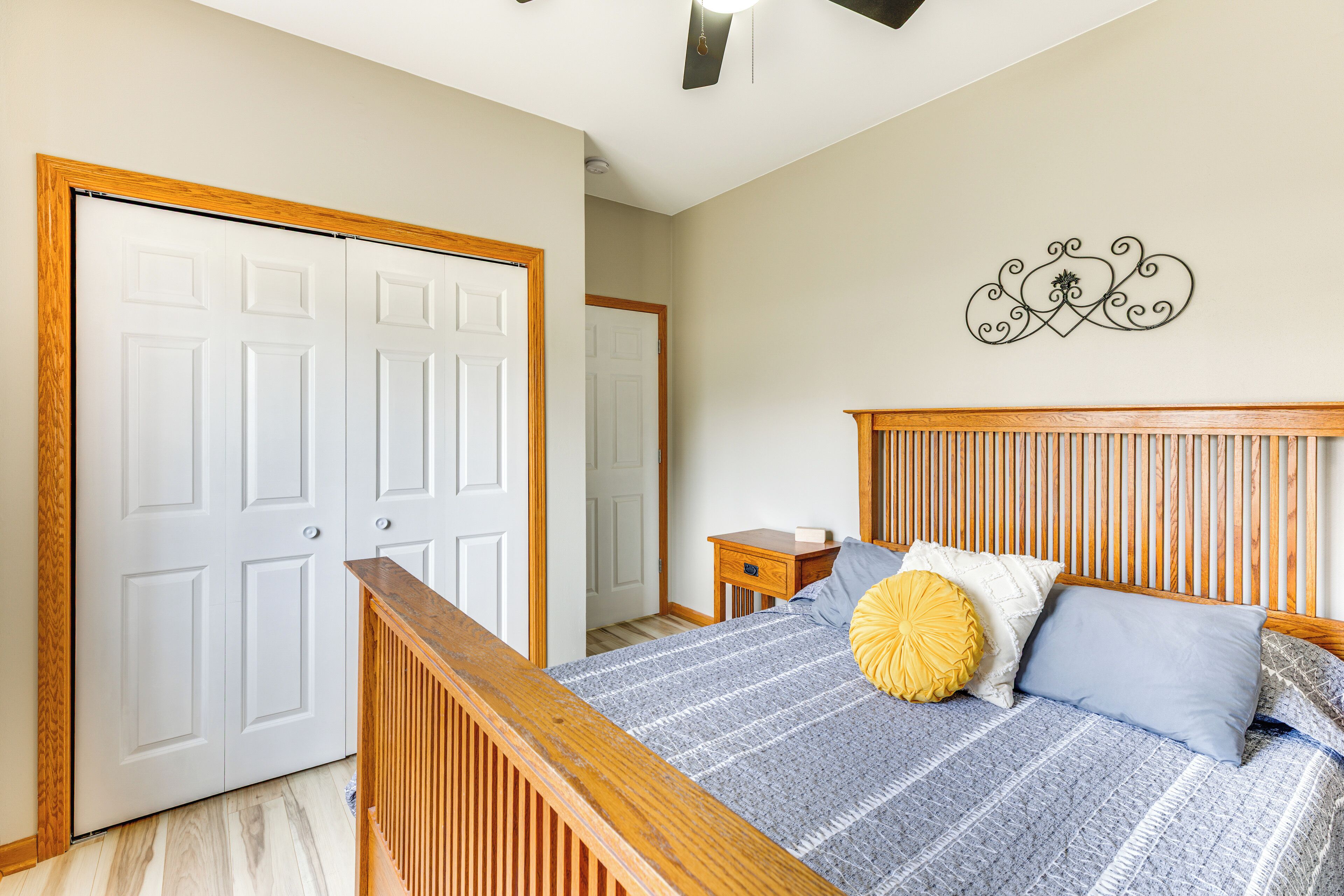 A bedroom with a wooden headboard, a bed with blue and white bedding, a yellow accent pillow, and a wall-mounted decorative piece.