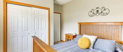 A bedroom with a wooden headboard, a bed with blue and white bedding, a yellow accent pillow, and a wall-mounted decorative piece.