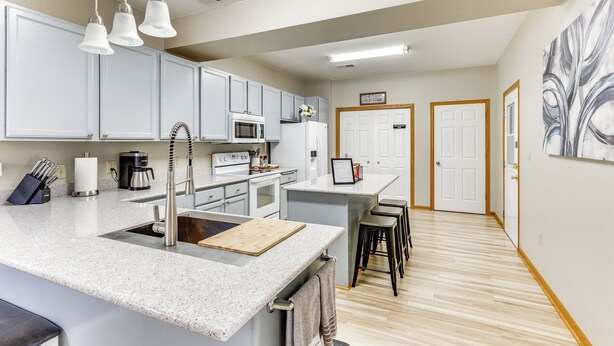 A modern kitchen with white cabinets, a granite countertop, and a central island with stools. There is a microwave, oven, and coffee maker on the countertop. - Lake Mills Retreat: 1 Mi to Beaches & Dining! (Lake Mills)