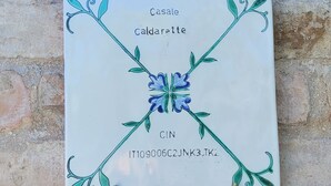 En keramisk platta med blommönster och text, monterad på en stenmur.