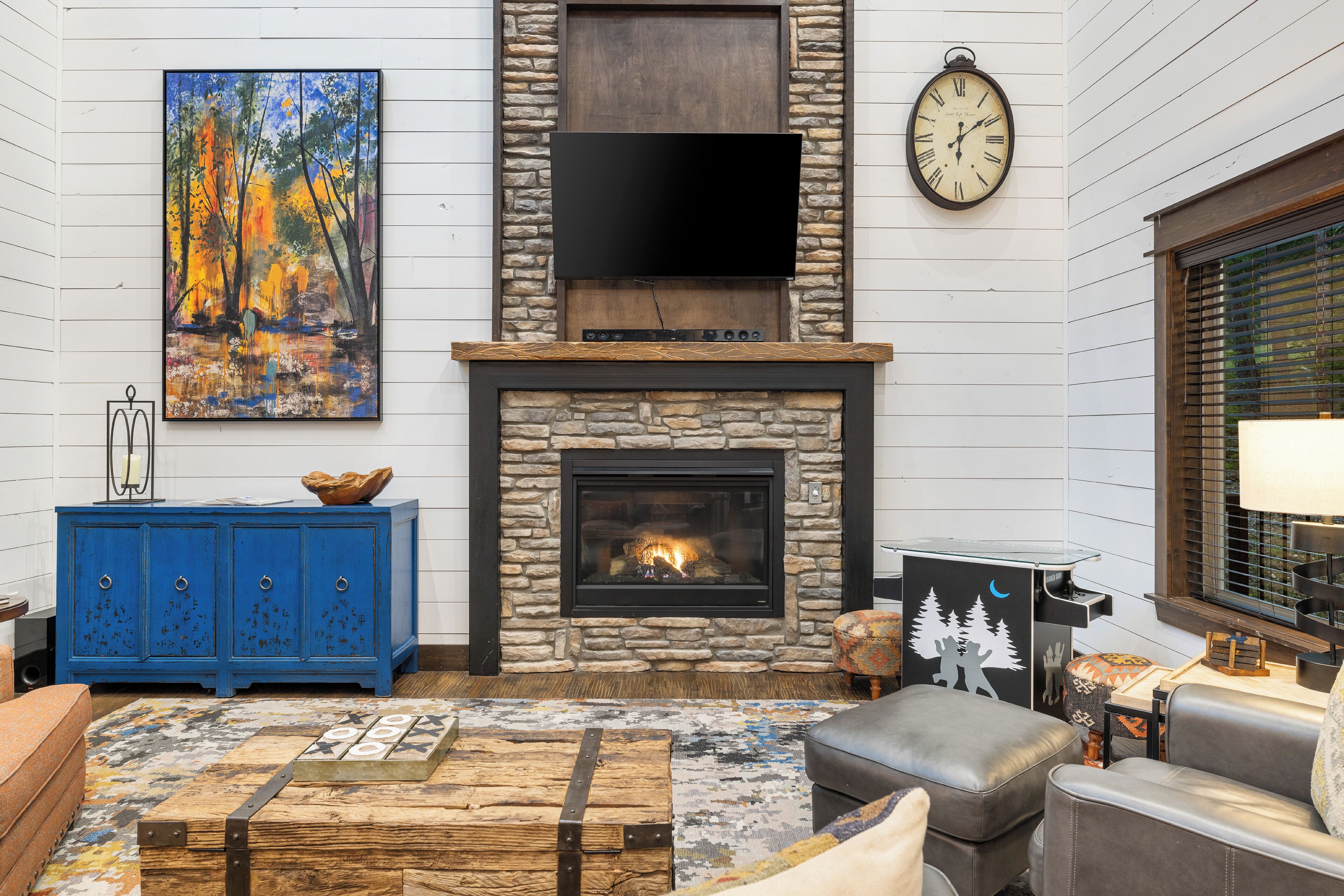 A living room with a stone fireplace, a flat-screen TV, a blue cabinet, and a colorful rug.