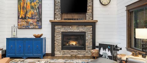 A living room with a stone fireplace, a flat-screen TV, a blue cabinet, and a colorful rug.