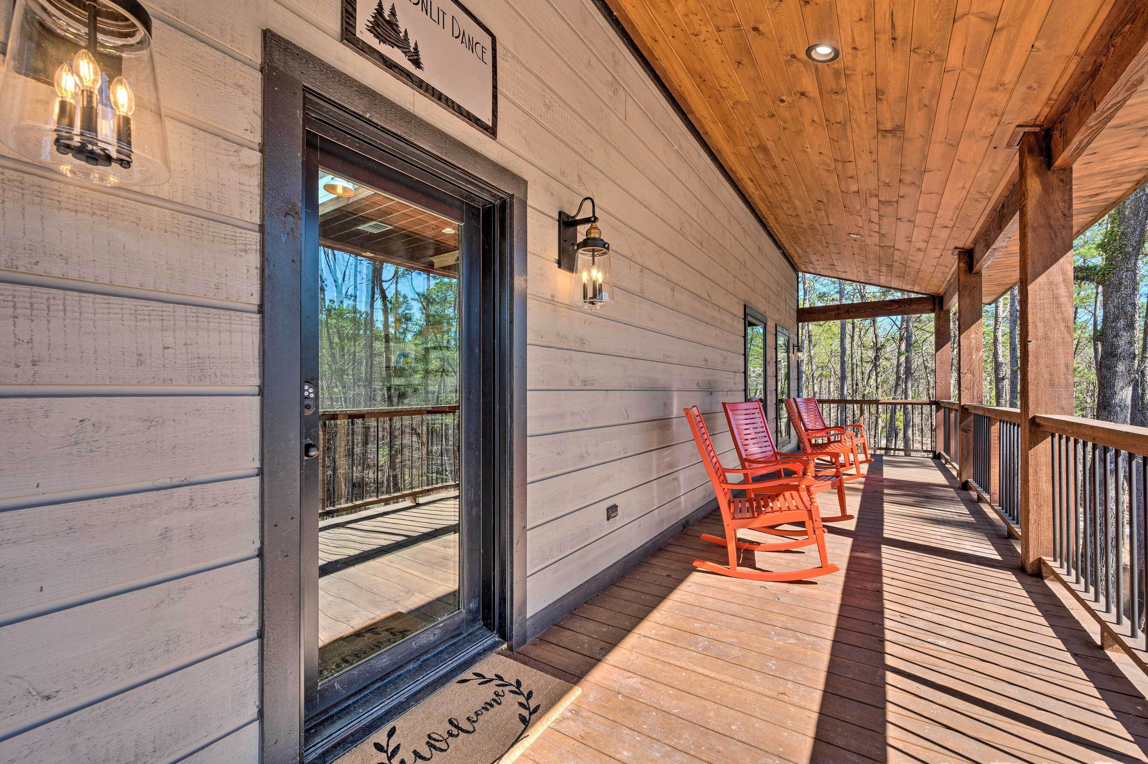 A wooden porch with a welcome mat, a sign above the door, and a view of the forest.