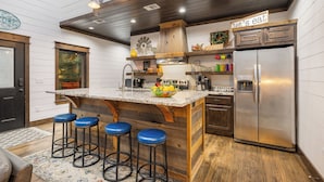 A kitchen with a wooden island, bar stools, a stainless steel refrigerator, and a 'Let's eat' sign.