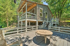Eine Holzhütte mit Balkon, Tisch und Stuhl auf einer Terrasse, umgeben von Bäumen.
