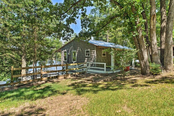 A rustic cabin with a wooden deck, surrounded by trees and a lake. - Waterfront Cottage in Fort Towson w/ 2 Decks! (Fort Towson)