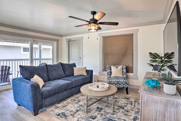 A modern living room with a blue sofa, a patterned armchair, a coffee table, and a ceiling fan. - Outdoor Dining, Steps to Sand: Indian Shores Condo (Indian Shores)