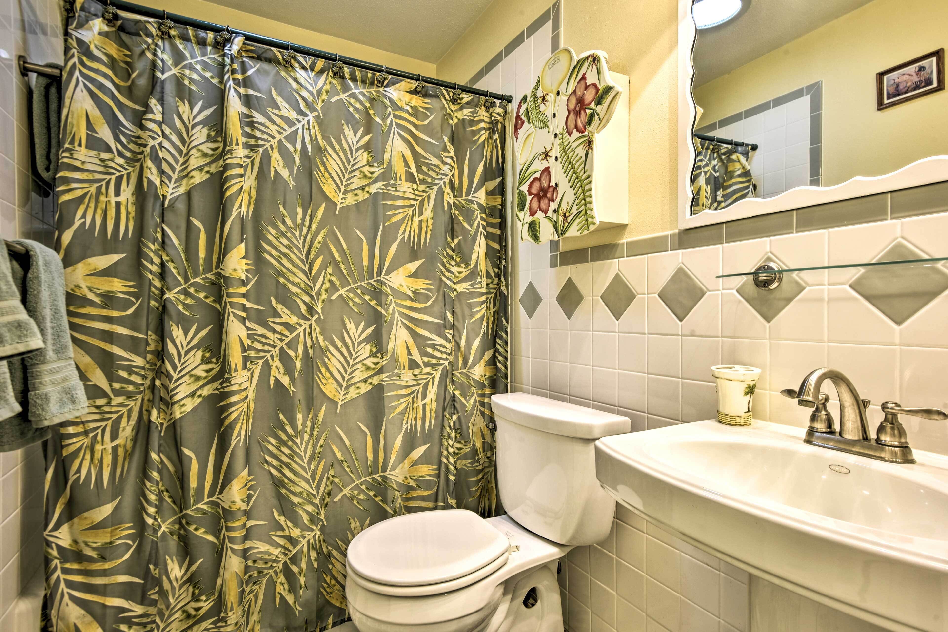 Un baño con inodoro, lavamanos y cortina de ducha con estampado de hojas tropicales.