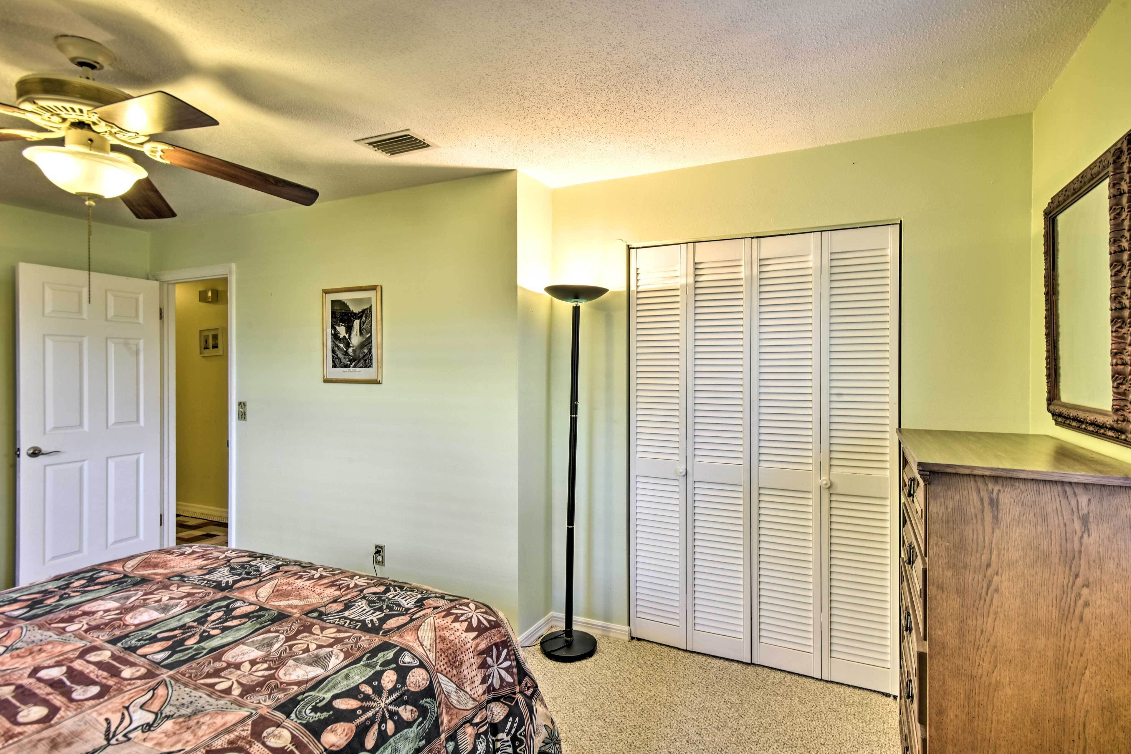 A bedroom with a bed, a ceiling fan, a floor lamp, a wardrobe, and a door leading to another room.