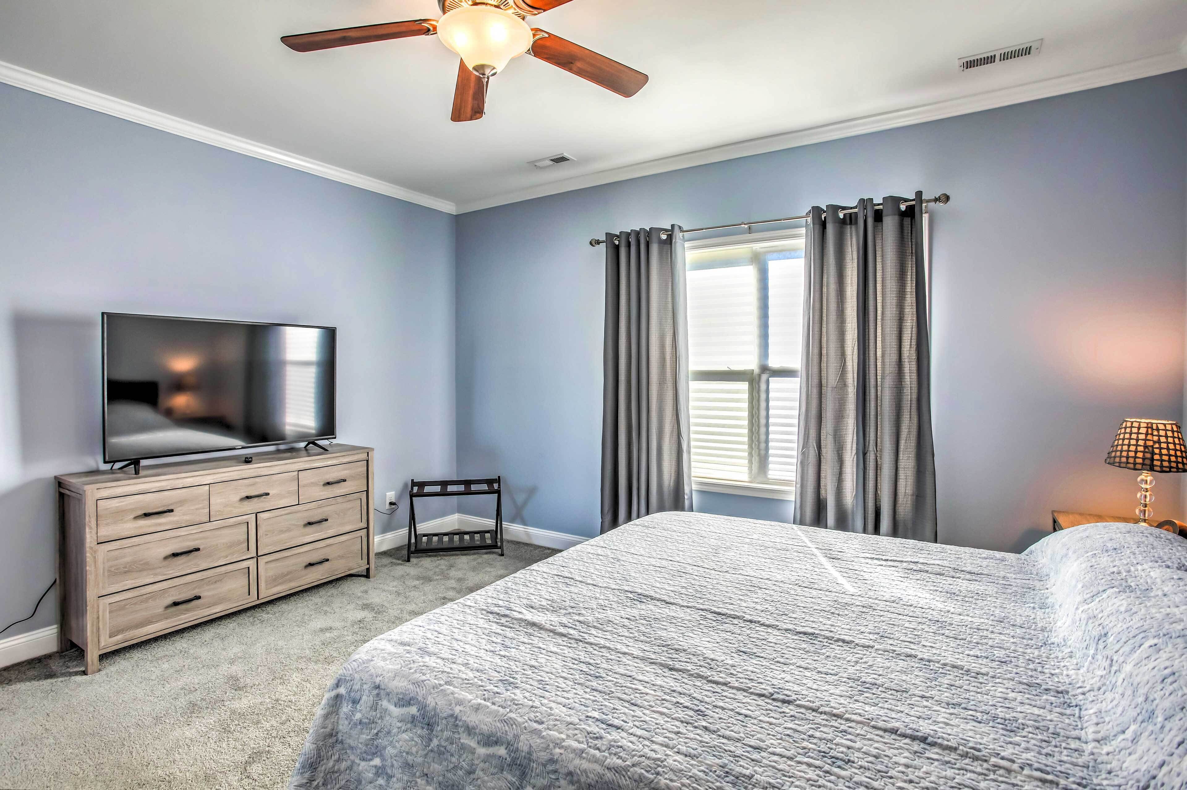 A bedroom with a bed, a dresser, a television, a ceiling fan, and a window with curtains.