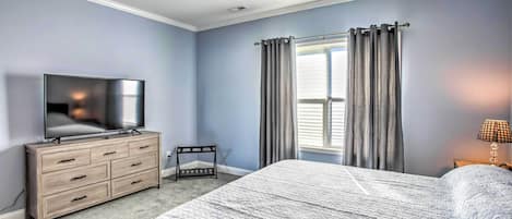 A bedroom with a bed, a dresser, a television, a ceiling fan, and a window with curtains.
