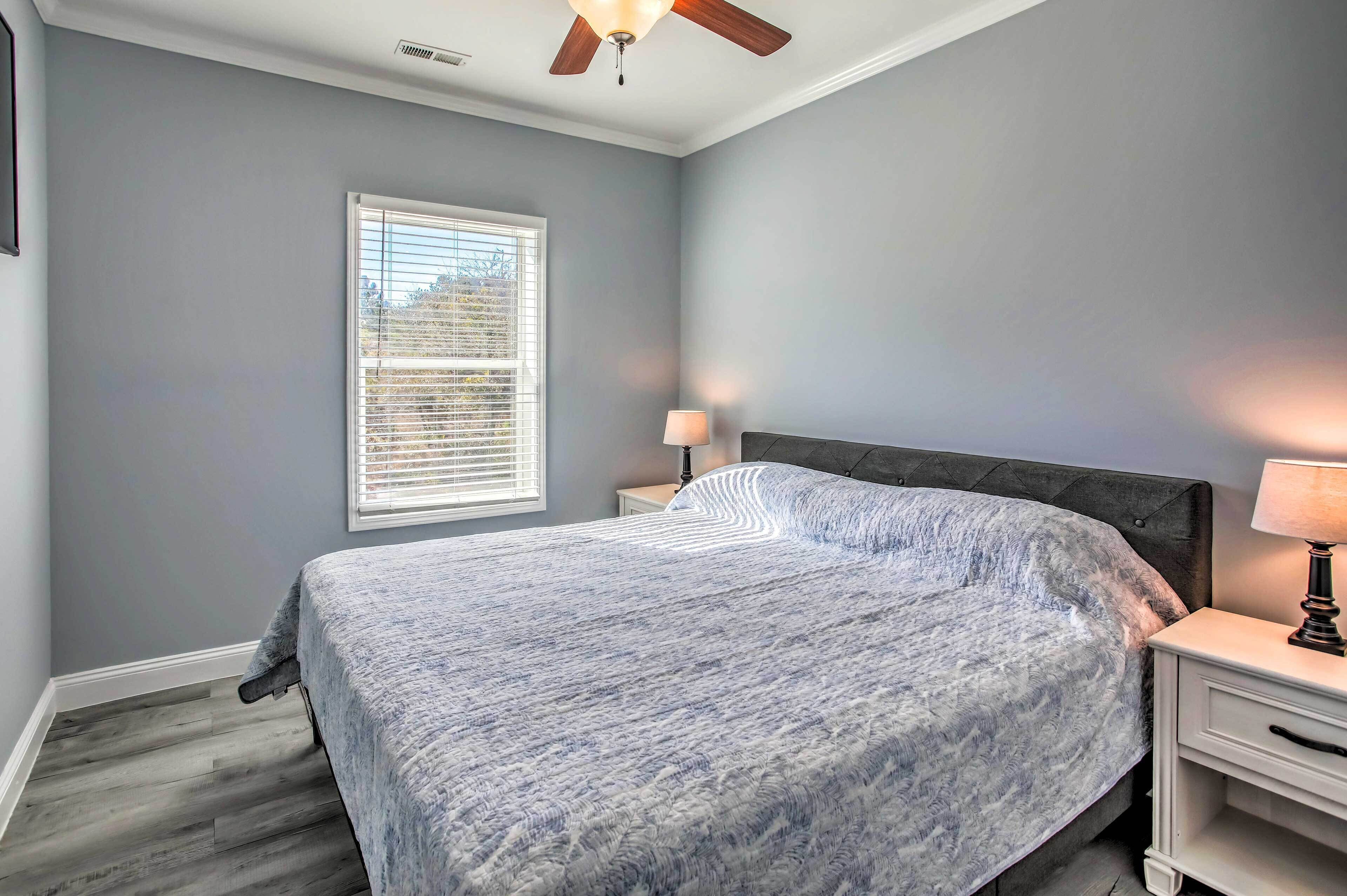 Ein Schlafzimmer mit Bett, Nachttisch, Lampe, Deckenventilator und einem Fenster mit Jalousien.