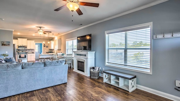 A spacious living room with hardwood flooring, a gray sofa, a fireplace, and a large window with blinds. - Ocean Isle Beach Escape - Centrally Located! (Ocean Isle Beach)