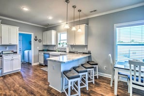 A modern kitchen with white cabinetry, a marble island, and pendant lighting.
