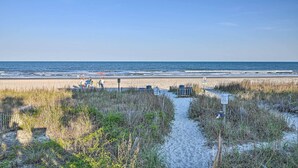 Ein Strandweg, der zum Meer führt, mit blauem Himmel.