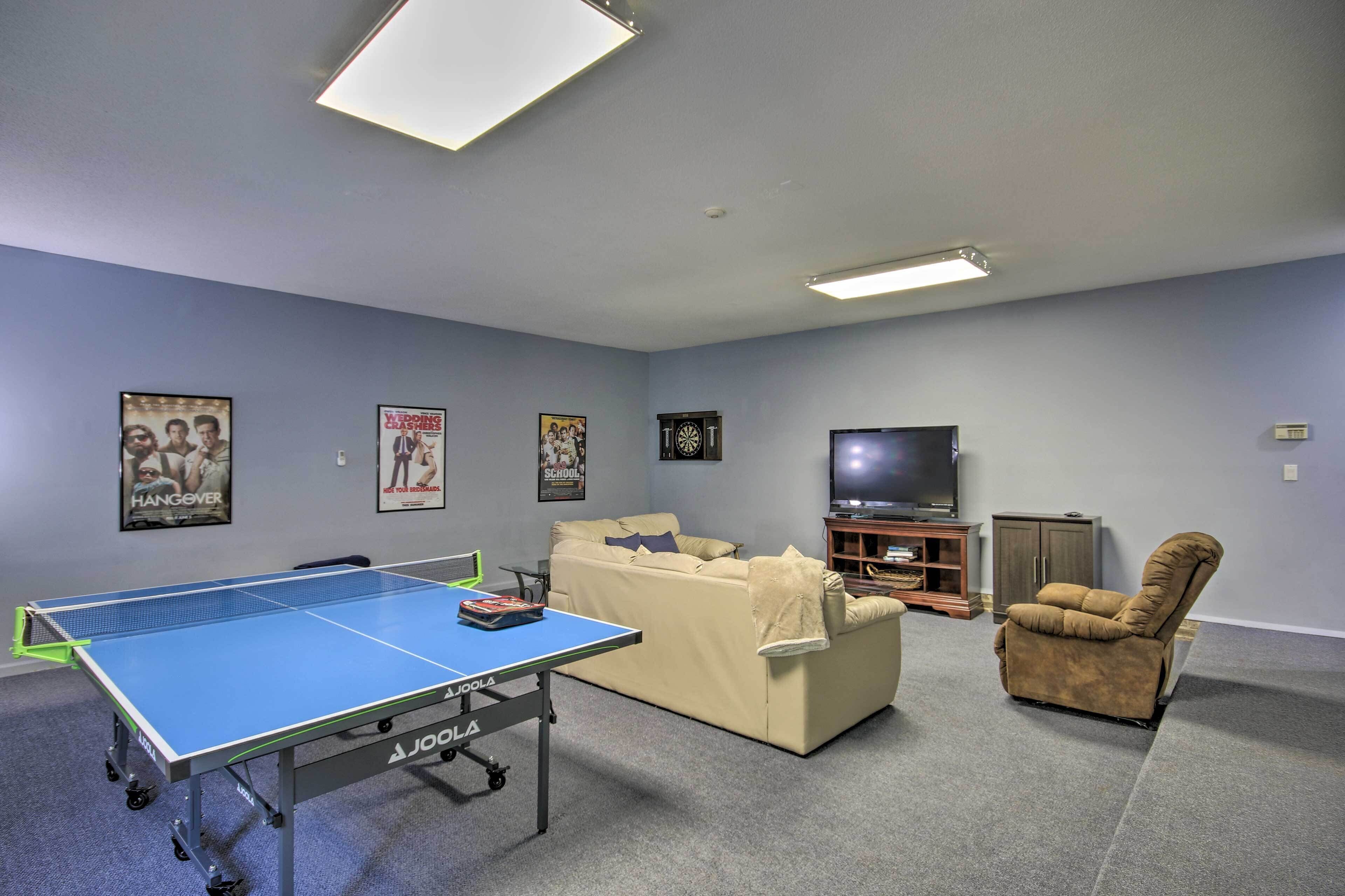 A room with a ping pong table, a sofa, a recliner, a television, and wall decorations.