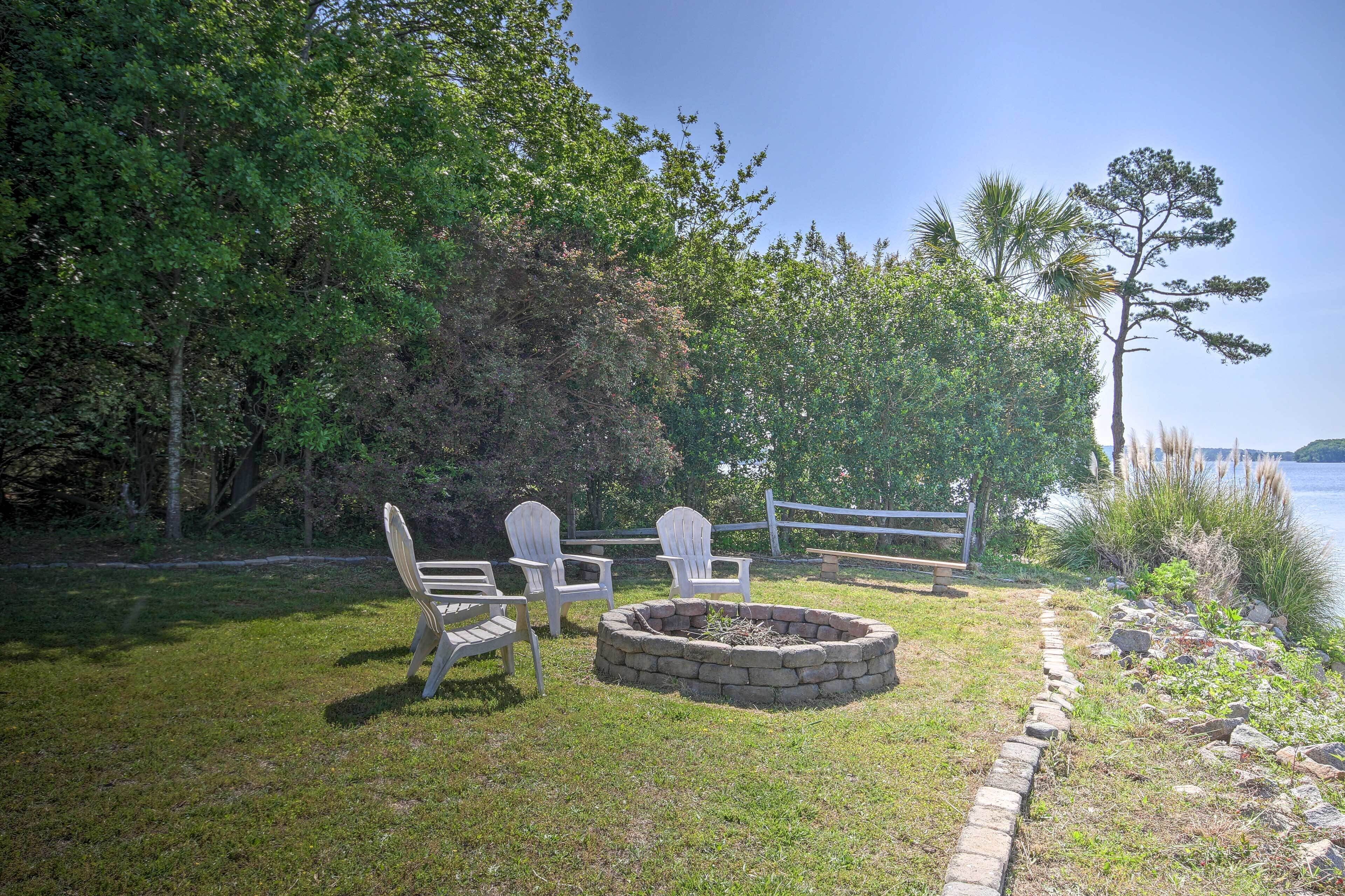 A grassy area with a fire pit, two Adirondack chairs, and a wooden bench.