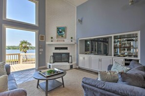 A living room with a fireplace, a large window overlooking a lake, and a view of the water. - Impeccable Home w/ Dock & Pool on Lake Wateree! (Camden)