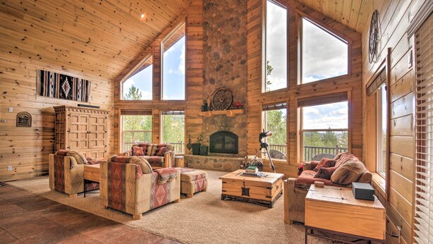 A spacious log cabin interior with a stone fireplace, large windows, and rustic furniture. - Gorgeous Alton Cabin w/ Deck + Mountain Views (Duck Creek Village)