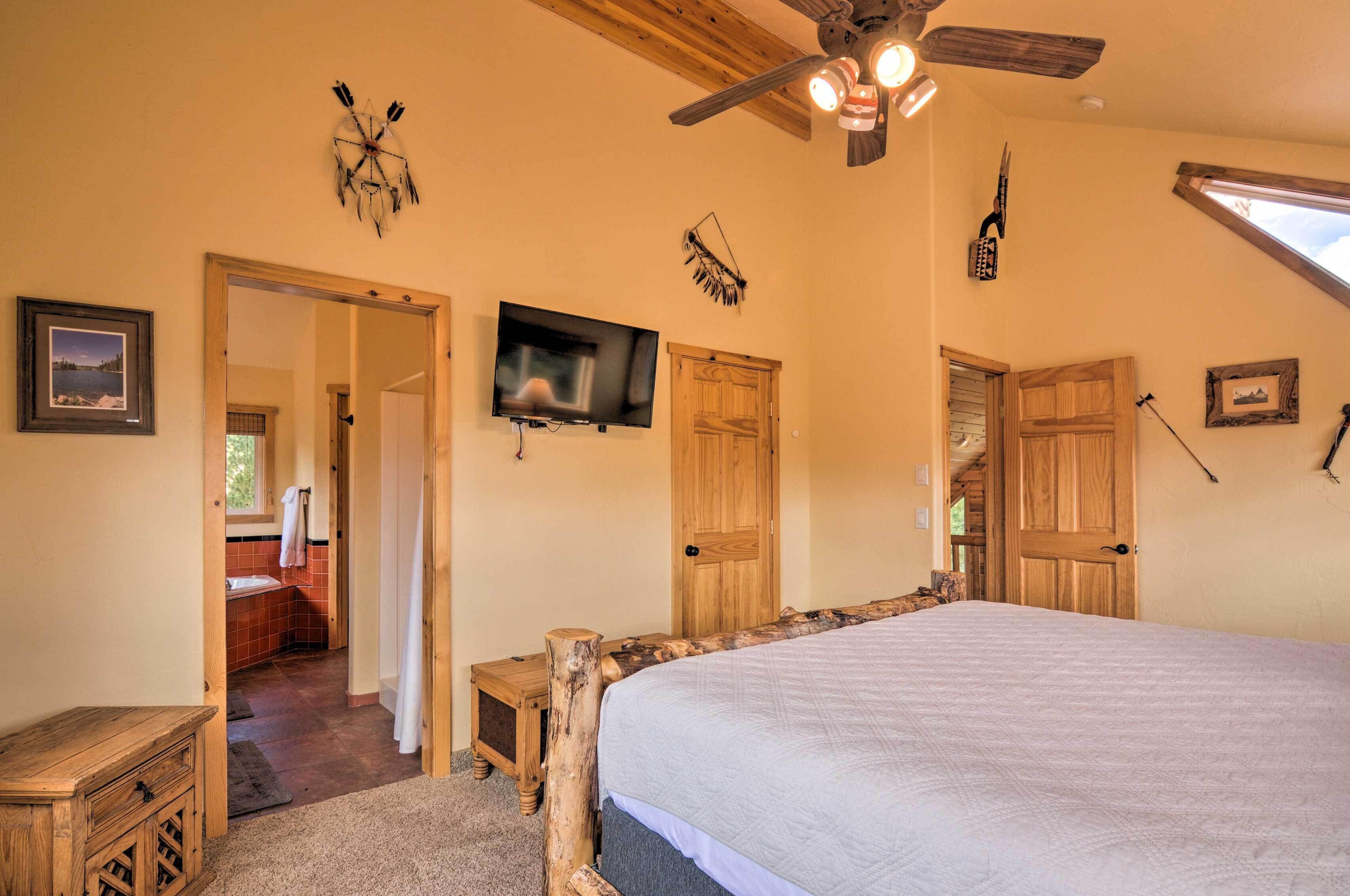 A bedroom with a large bed, wooden doors, a ceiling fan, and a TV on the wall.