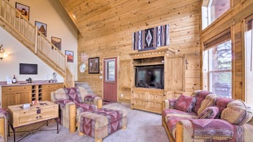 A log cabin interior with a wooden staircase, a TV, and patterned furniture.