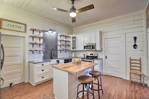 A kitchen with white cabinets, a wooden island with stools, a ceiling fan, and a 'PANTRY' sign.