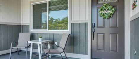 A porch with two chairs and a table, a door with a wreath, and a welcome mat.