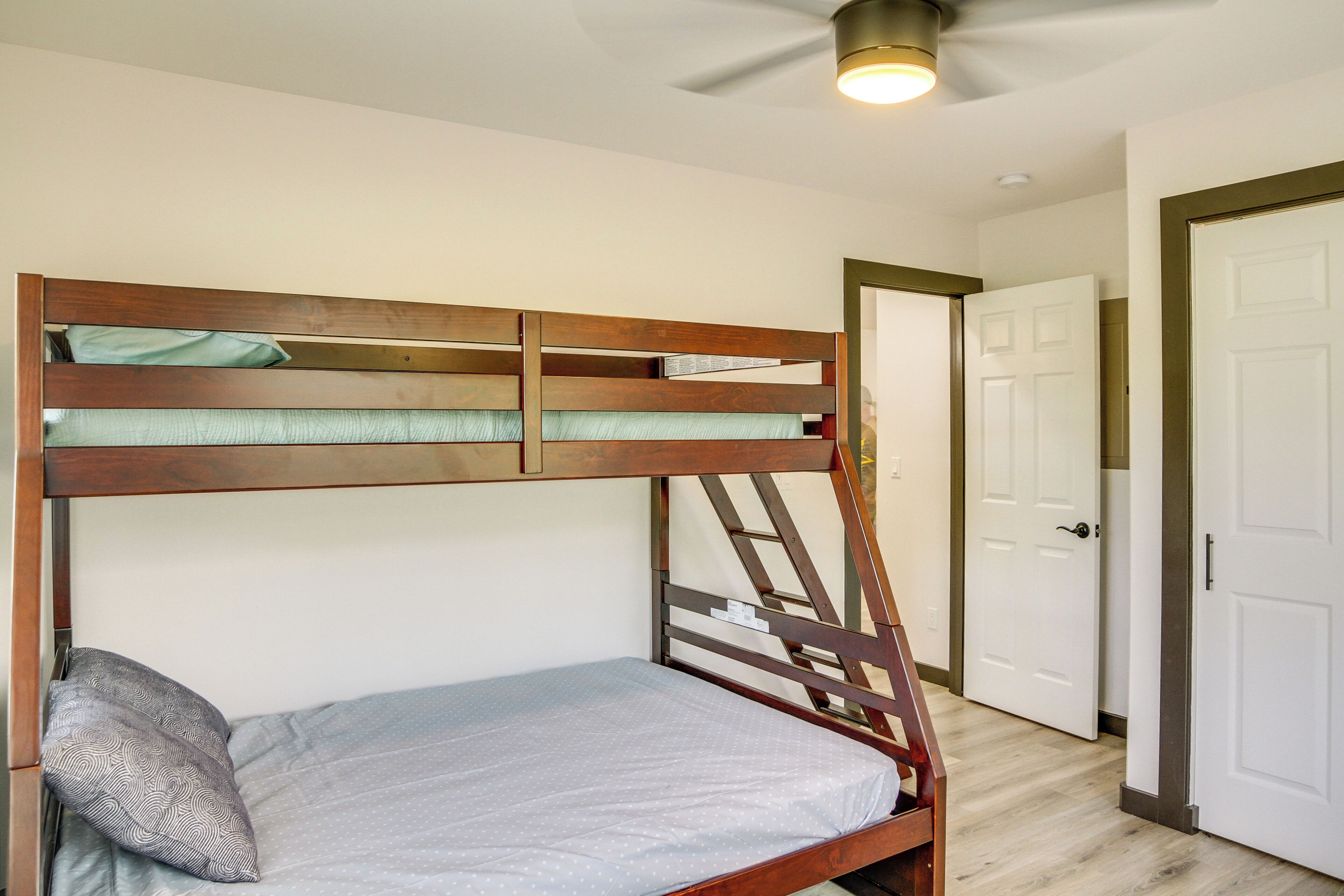 A bunk bed with a ladder, a single bed, and a ceiling fan in a room with wooden flooring and white walls.