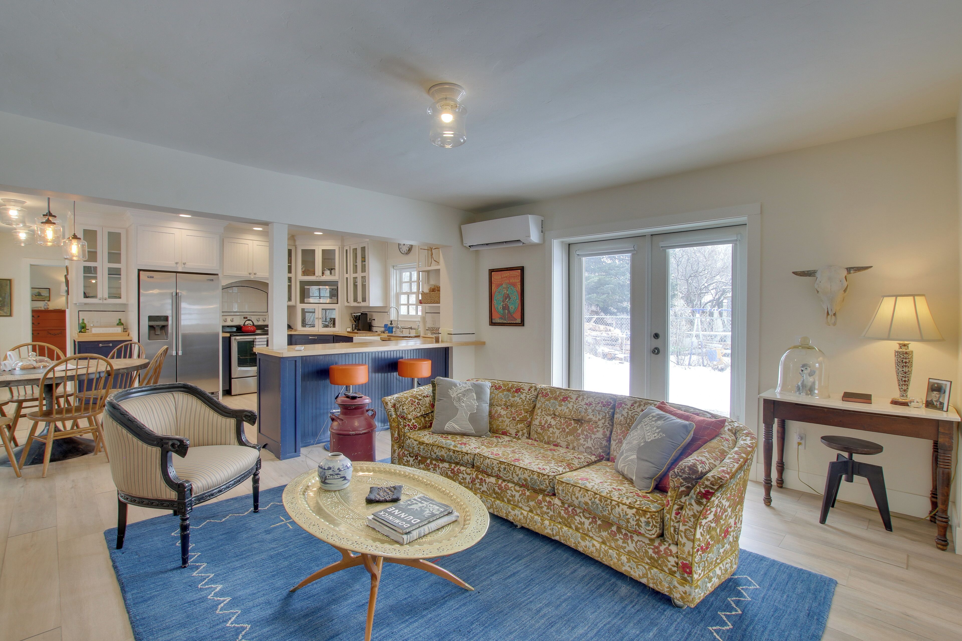 A spacious living area with a sofa, coffee table, and dining set. A kitchen with modern appliances and a dining area with chairs and a table are visible.