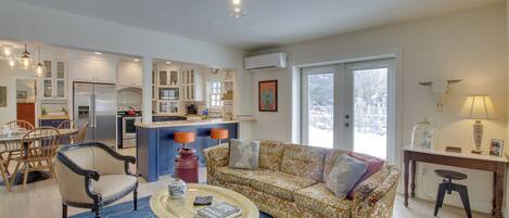 A spacious living area with a sofa, coffee table, and dining set. A kitchen with modern appliances and a dining area with chairs and a table are visible.